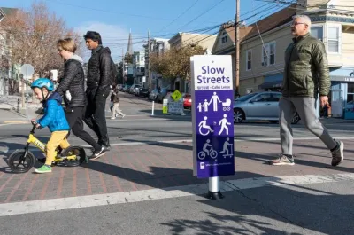 White and purple sign for Slow Street in San Francisco, California with people crossing crosswalk.