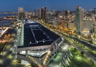 The San Diego Convention Center is illuminated at night with the backdrop of public transit lines and high-rise buildings.