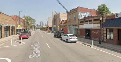 A view up Santa Fe Drive in Denver. Stores and construction are visible along the street, and Downtown Denver looms in the background.