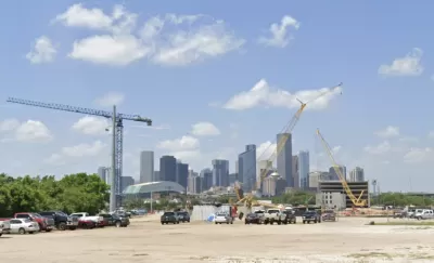 Dirt lot with construction cranes and parked cars with downtown Houston skyline in background