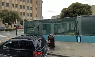 Google street view of tiny home village behind see-through green fence at 33 Gough St. in San Francisco with brick building in background
