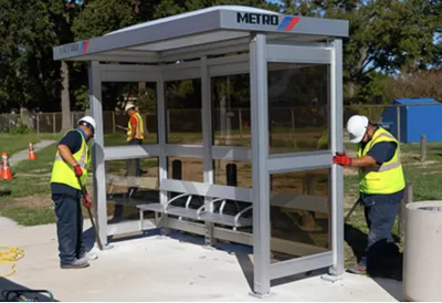 Workers in yellow safety vests installing a bus station shelter in Houston, Texas.
