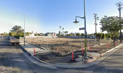 Google street view of vacant fenced-in dirt lot in South Los Angeles with graffiti on wall in background.
