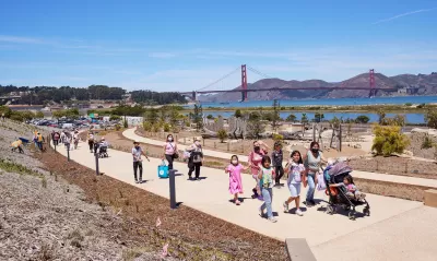 People walking on a concrete pathway at Presidio Tunnel Tops with the Golden Gate Bridge in the background