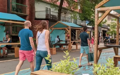 Pedestrians walk down car-free Mont-Royal Avenue next to green outdoor dining kiosks in Montreal, Canada