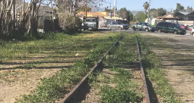 Old railroad line overgrown with grass with cars parked in background