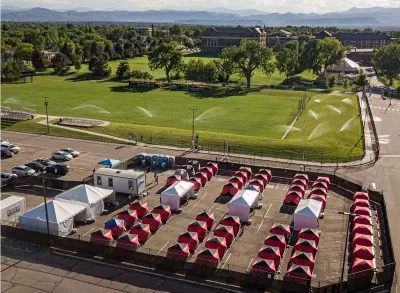 Ice fishing tents surrounded by fence in Safe Outdoor Space for unhoused people in parking lot in Denver, Colorado.
