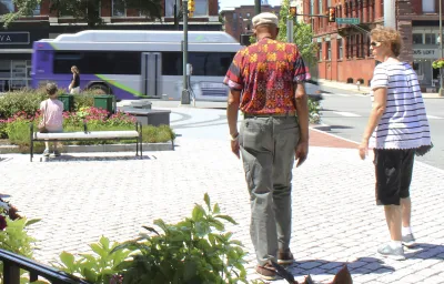 Two people walking away from camera through pedestrian plaza in street in Richmond, Virginia with purple and white city bus moving in background.