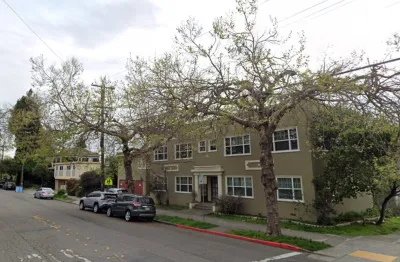 Two-story green apartment building in residential neighborhood in Berkeley, California with tall street trees.