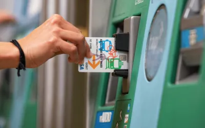 Close-up of hand inserting Mobility Wallet card into green Los Angeles Metro ticketing machine.