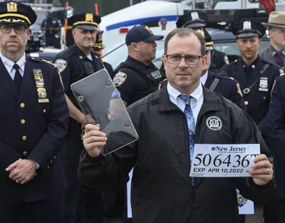 New York City police official holding up paper license plate and clear cover at press conference.