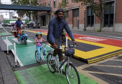 Dad and small kids ride bikes on colorful bike lane next to bus lane protected with low buffers in Portland, Oregio.