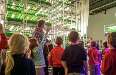 Man showing tour group of children indoor farming with automated planting shelves.