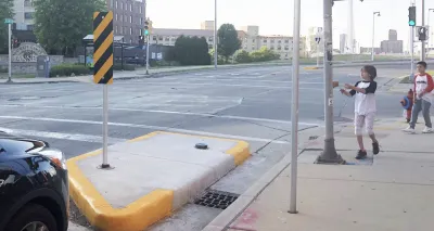 Two children stand on sidewalk at crosswalk with yellow curb extension.