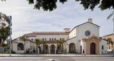Spanish Revival building in Los Angeles, former mortuary turned apartments with two people walking and one biking by in front.