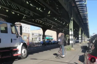 Cyclist rides along 31st street in New York City next to elevated train track.