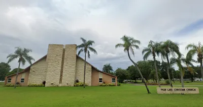 Google street view of modernist tan-colored triangular church building with tall skinny palm trees in front with green lawn in St. Petersburg, Florida.