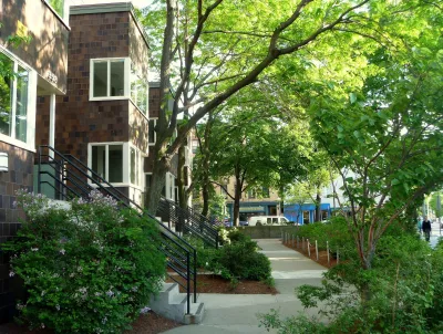 Two-story public housing building with dark red wood cladding on leafy street in Cambridge, Massachusetts.