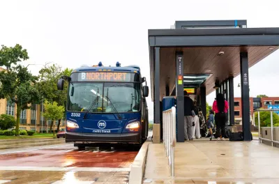 Blue transit bus stopped at outdoor station with covered platform in Madison, Wisconsin.