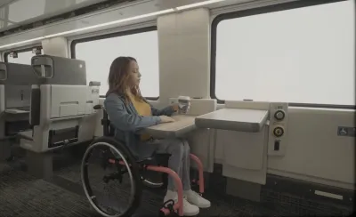 Woman in wheelchair sits at table next to window on Amtrak train.