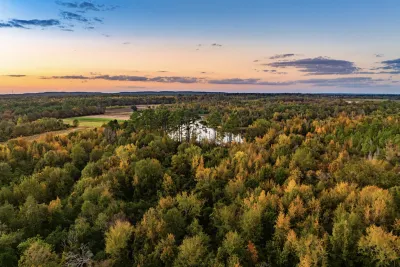 An aerial view of the new state park, with a forest and lake visible under a sunset.