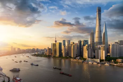 A view of Downtown Shanghai's skyscrapers, rising above a Huangpu River full of boats leaving wakes visible in the fading light of sunset.