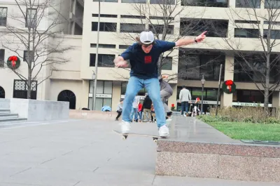 Boy wearing jeans and white cap skateboards off marble ledge in Freedom Park, Washington DC.