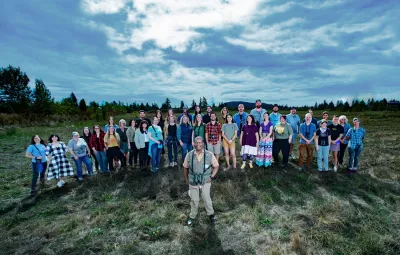 A crowd of people look up at a camera on the field that will become a nature sanctuary.