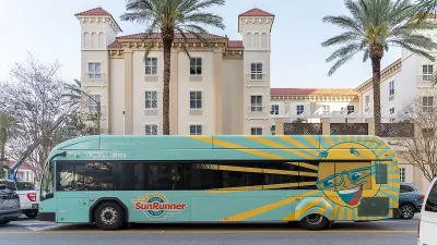 Teal and yellow Sunrunner bus in front of Spanish-style building and palm trees in St. Petersburg, Florida.