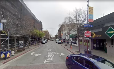A narrow, one-way street is lined with businesses.