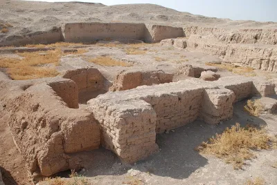 A pile of tan rocks form a wall at the ruins of Tell Brak. They are surrounded by yellow grass.