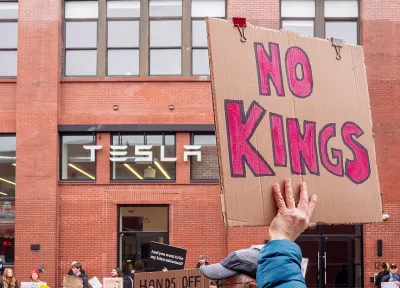 Close-up on cardboard sign reading 'No Kings' being held up at protest at Tesla offices in Brooklyn, New York.
