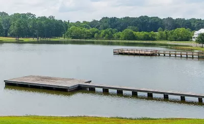 View of docks on lake surrounded by green trees and lawns with one white house at right