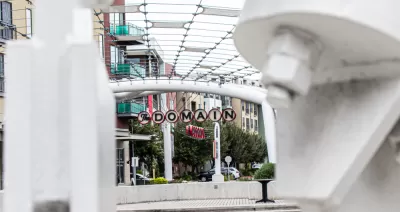A picture of a decorative sign announcing “The Domain” surrounded by high density shops and apartments.