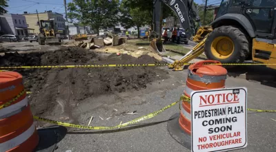 Pedestrian plaza construction site with orange cones and excavator in Jersey City, New Jersey.