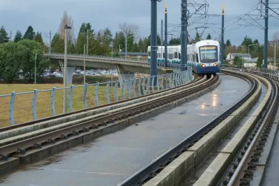 A Link light rail transit train navigates a corner with an empty field and parked cars in the background.