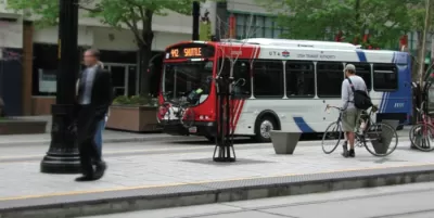 White, red, and blue Utah Transit Authority bus at stop with man standing on sidewalk next to bicycle