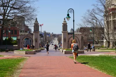 An image of the Sample Gates at the entrance of the college campus of Indiana University Bloomington, with a street and the city in the background. 