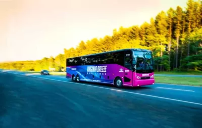 Purple Virginia Breeze intercity bus driving down blurred road with trees on roadside.