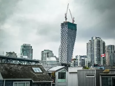 View of Vancouver House skycraper under construction with two cranes at top and other downtown Vancouver buildings surrounding it against a grey sky
