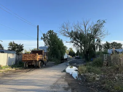 Small paved street with yellow dump truck parked on side and puddle on shoulder in Brooklyn.