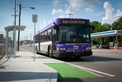 Purple buss pulls up to bus stop in green bus lane.