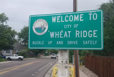 A road sign reads "Welcome to City of Wheat Ridge Buckle Up and Drive Safely"