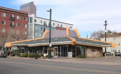 The sloped roof of a googie style building is prominently featured in this image of a restaurant in Denver. Tall apartment buildings are seen in the background.