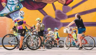 Group of cyclists wearing helmets pause in front of a mural in El Paso, Texas.
