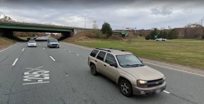 A two-lane highway cuts through a small canyon. The photo is taken from the perspective of a vehicle on the road.