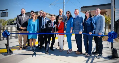 A group of smiling people cut a blue ribbon in front of Sacramento's new light rail station.