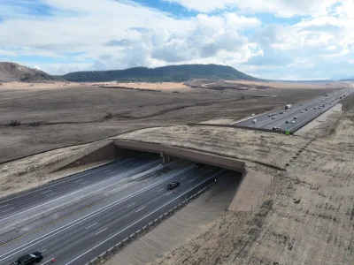 The largest wildlife overpass in North America stretching over the I-25. Both sides of the overpass, and the overpass itself, are covered in brown grass.
