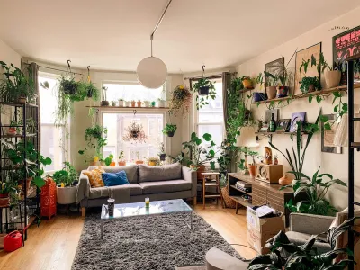 A living room in Logan Square, Chicago, IL with white walls and large windows filled with lots of plants and furniture.