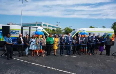 A crowd of people in front of two MetroNow buses, cutting a blue ribbon.